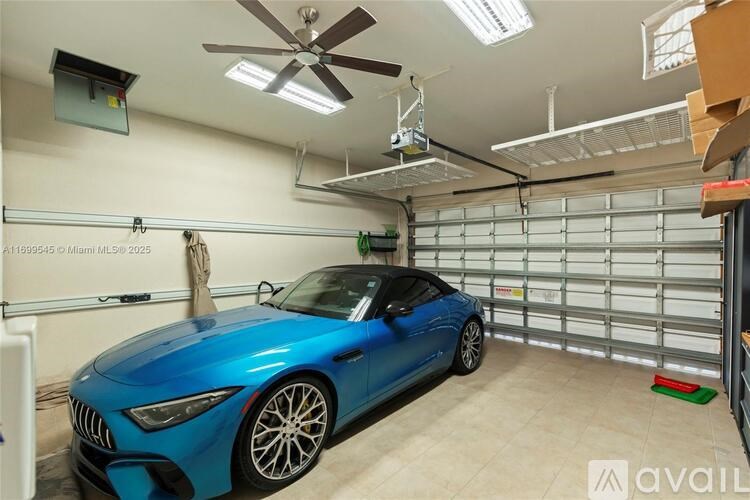 A blue sports car is parked in a garage with a ceiling fan overhead.