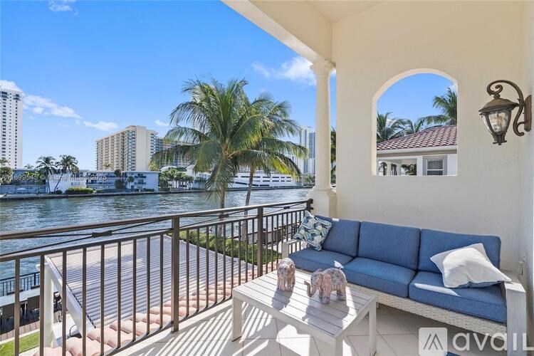 A balcony with a sofa and a table overlooking a body of water with buildings in the background.