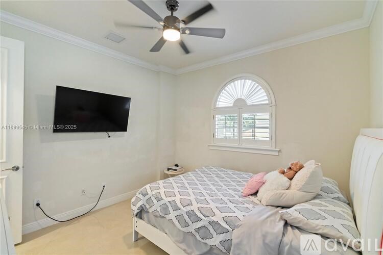 A bedroom with a bed, a ceiling fan, and a flat-screen TV mounted on the wall.