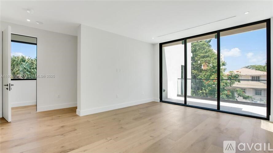 A spacious room with wooden flooring and large windows overlooking a garden.