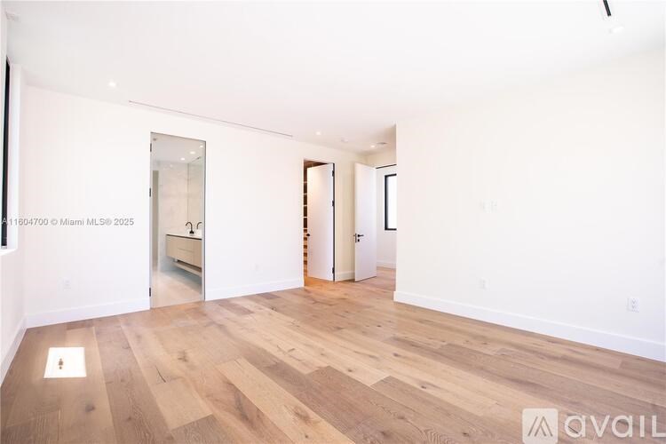 A room with wooden flooring and white walls, with a mirror on the left wall and a door on the right.