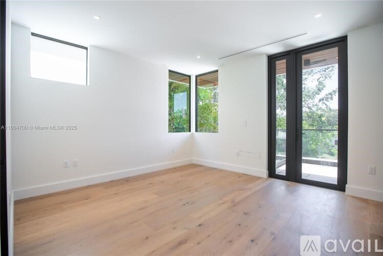 A large empty room with wooden floors and a sliding glass door leading to a garden.