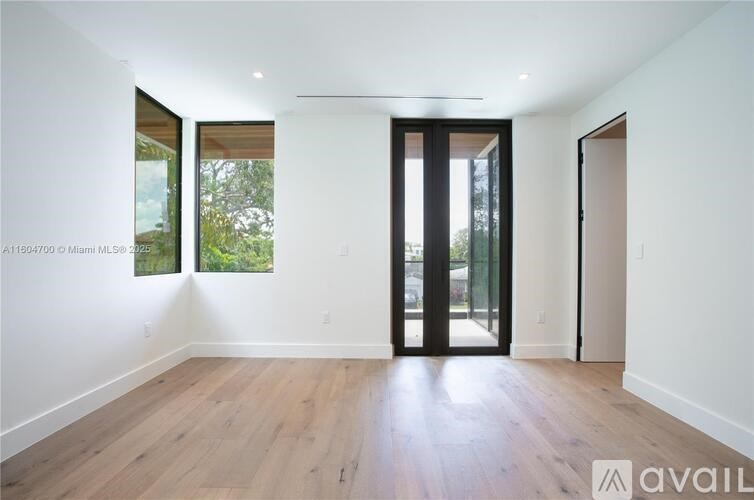 A room with wooden floors and white walls, with a large window and a door.