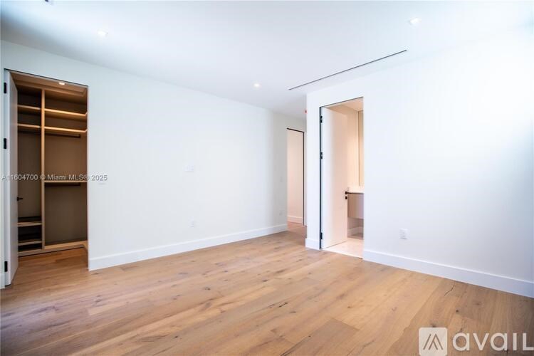 A room with wooden flooring and white walls, with a door on the right side.