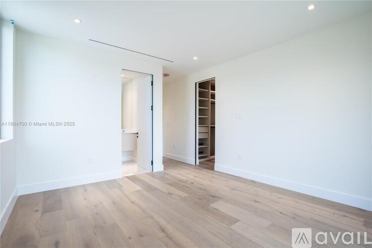 A room with wooden flooring and a white wall with a doorway leading to another room.