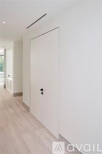 A white door with a black handle is in a hallway with wood floors and white walls.