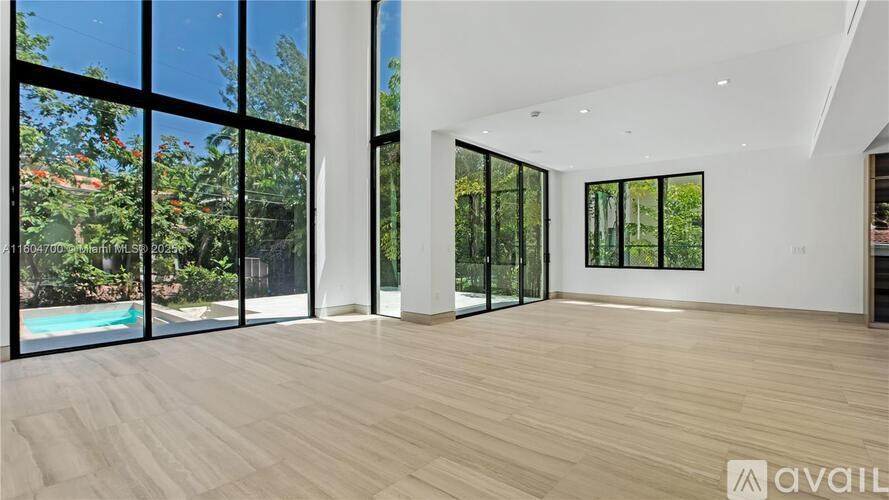 A spacious room with wooden flooring and large windows overlooking a pool and greenery.