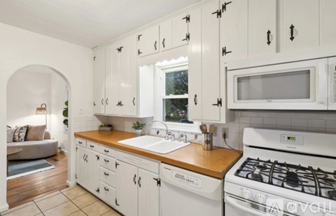 A white kitchen with a wooden counter top and white cabinets.