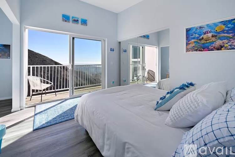 A bedroom with a large bed and a view of the ocean through the sliding glass doors.