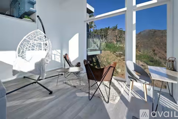 A white chair with a black metal frame is in the foreground of a sunny room with a mountain view.