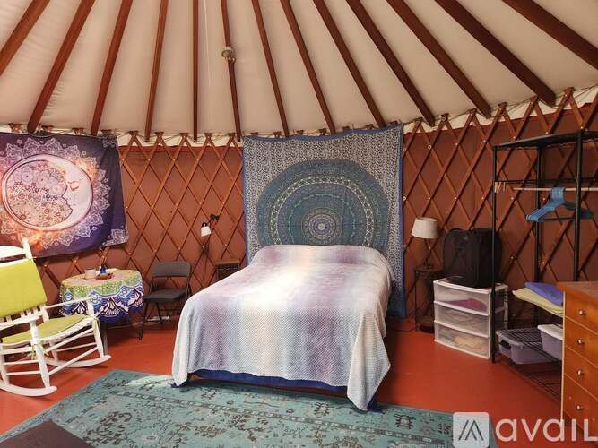 A bedroom with a bed, chair, and rugs inside a yurt.