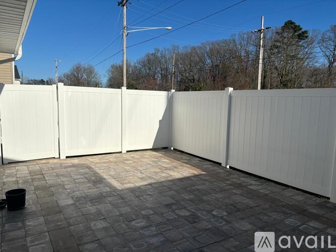 A backyard with a white fence and a black bucket on the ground.