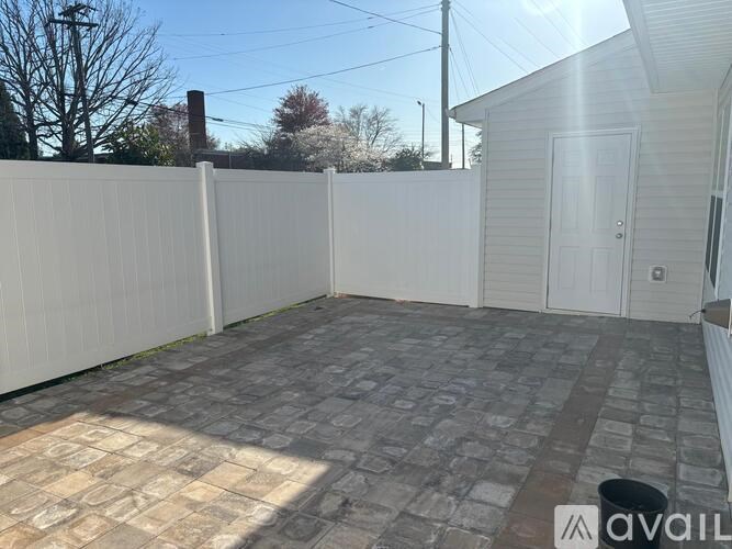 A backyard with a white fence and a brick patio.
