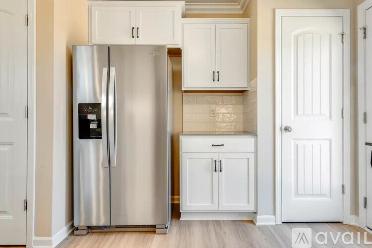 A stainless steel refrigerator is in a kitchen with white cabinets.