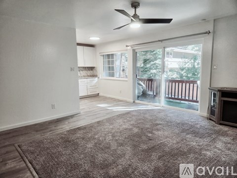 A living room with a grey carpet and a ceiling fan.