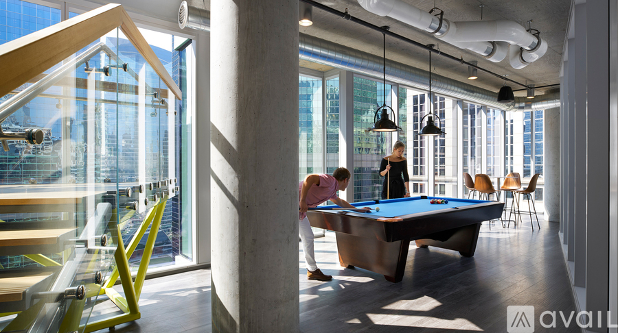 A pool table in a room with a person standing behind it.