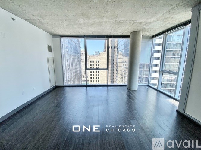 A spacious room with wooden floors and large windows overlooking a cityscape.