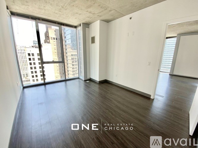 A spacious room with wooden floors and large windows overlooking a cityscape.
