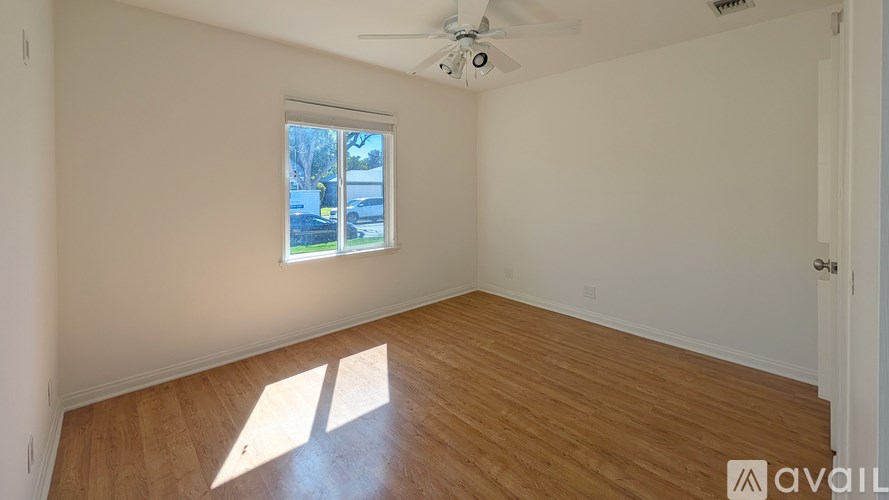 A room with wooden flooring and a window showing a view of a lawn and trees.
