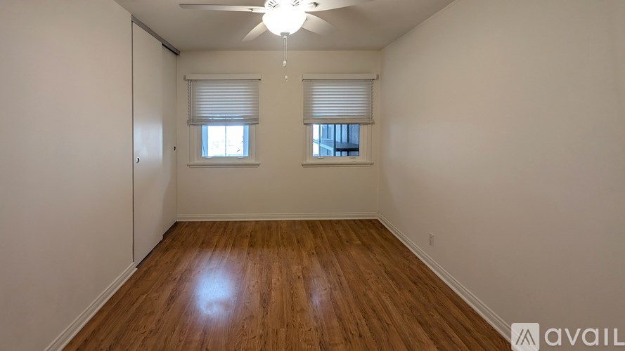 A room with wooden flooring and two windows with blinds.