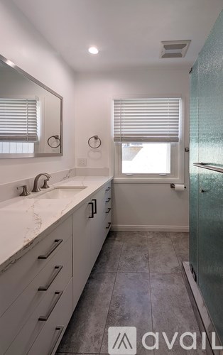 A bathroom with a sink, mirror, and a window with blinds.