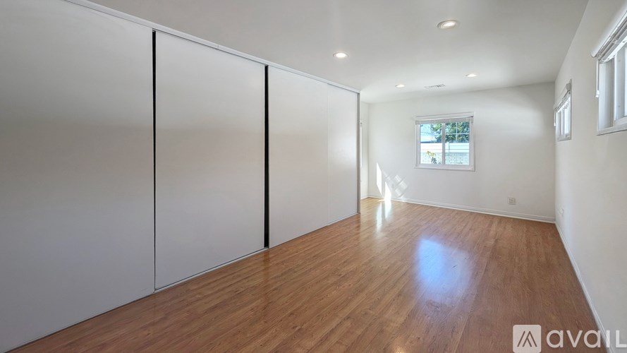A room with wooden flooring and white walls, with a window on the right wall.