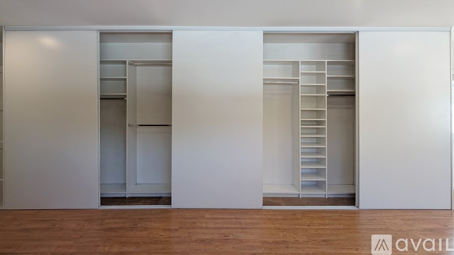 Three white closets with shelves and drawers are in a room with wooden floors.