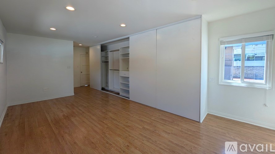 A room with wooden floors and white walls, with a window on the right side.