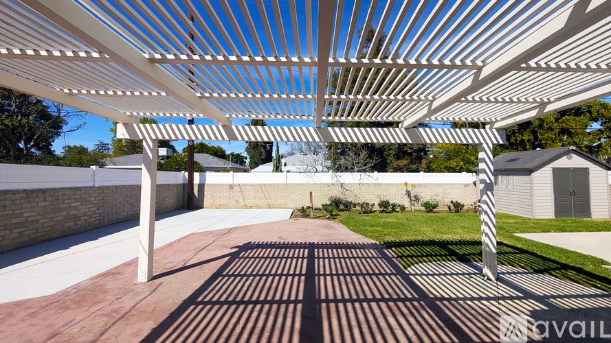 A white pergola with a striped canopy over a brick patio.