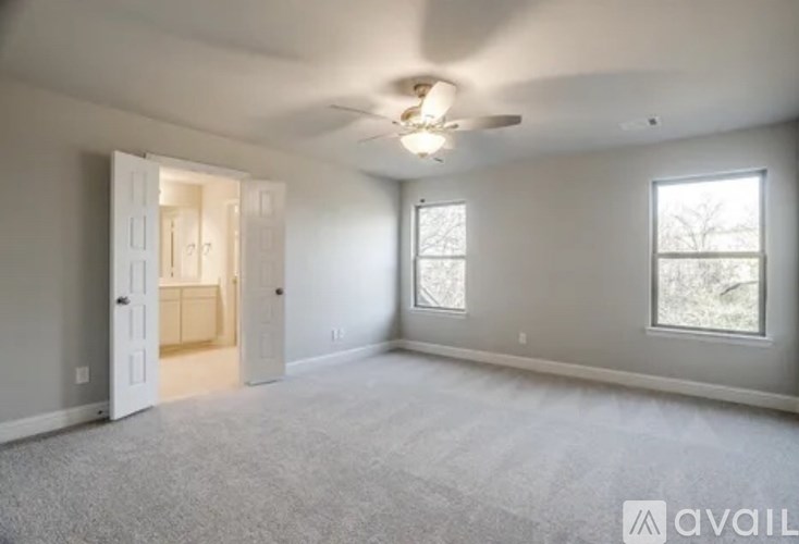 A spacious room with a carpeted floor, a ceiling fan, and two windows.