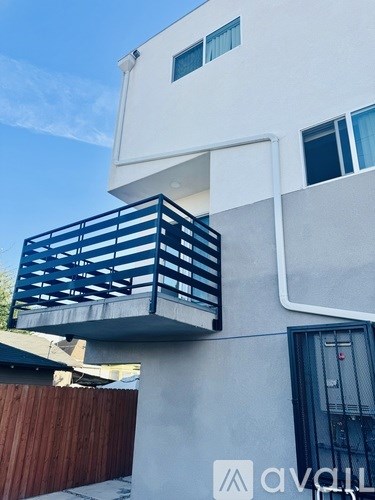 A modern white building with a balcony and a black door.