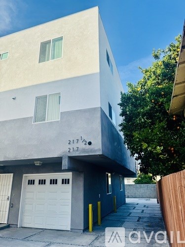 A modern two-story building with a garage door and a tree in front.