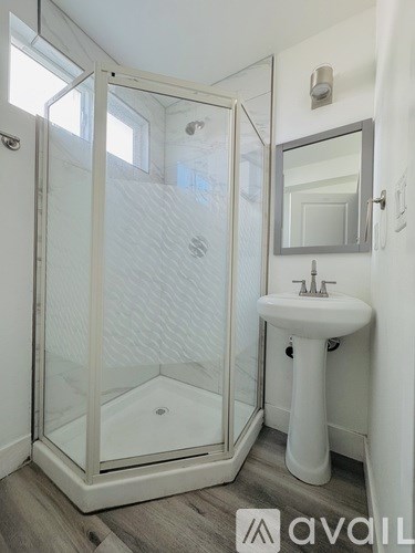 A white pedestal sink sits under a mirror in a bathroom with a walk-in shower.