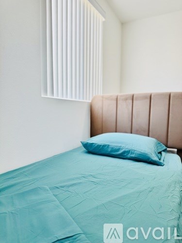 A bed with a teal comforter and a blue pillow with a white wall in the background.