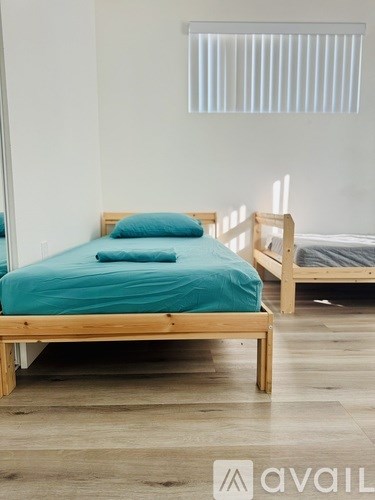A bed with a teal comforter and a blue pillow is in the foreground of a room with a second bed in the background.