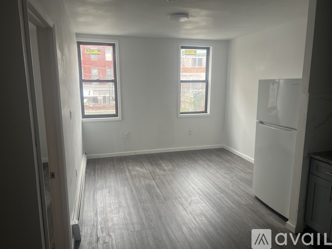 A room with a white fridge and two windows.