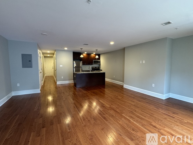 A spacious room with wooden flooring and a kitchen area in the background.