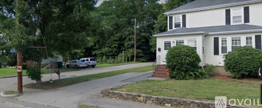 A house with a white exterior and a grey roof is situated on a street with a car parked in front.