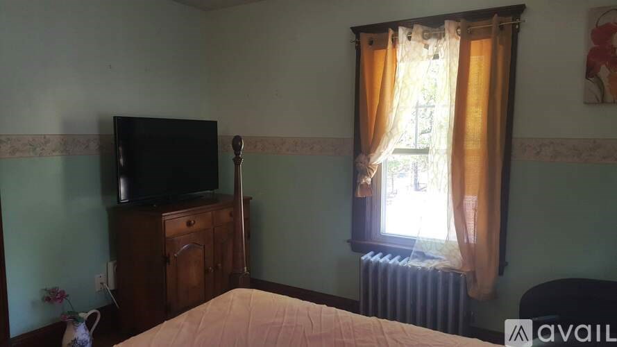 A bedroom with a bed, a television, and a window with curtains.