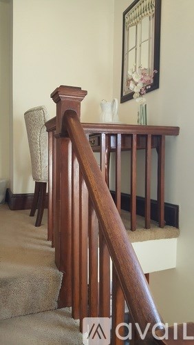 A wooden staircase with a carpeted runner and a chair with a beige cushion.