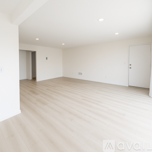 A spacious room with wooden flooring and white walls.