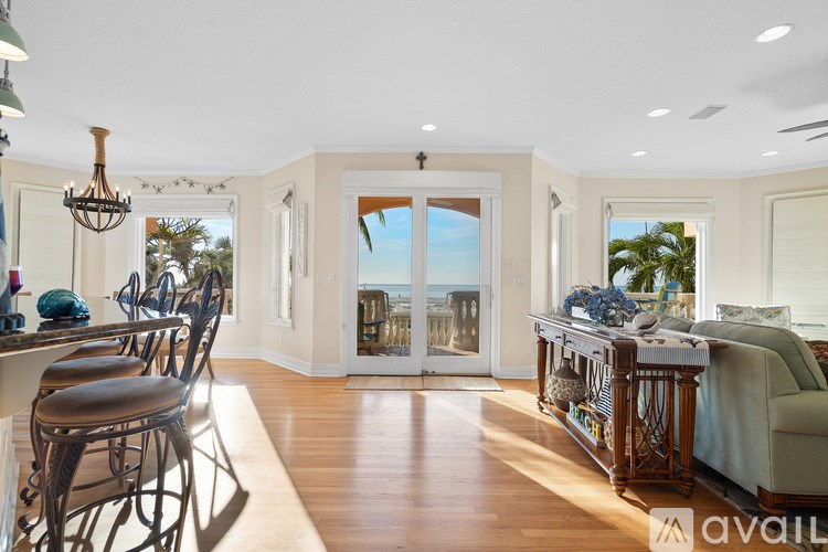 A well-lit room with a dining table and chairs, a sofa, and a bed with a view of the ocean through a sliding glass door.