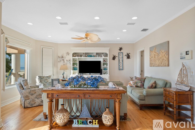 A living room with a TV, a sofa, a chair, a table with a vase of flowers, and a rug with the word "BEACH" on it.