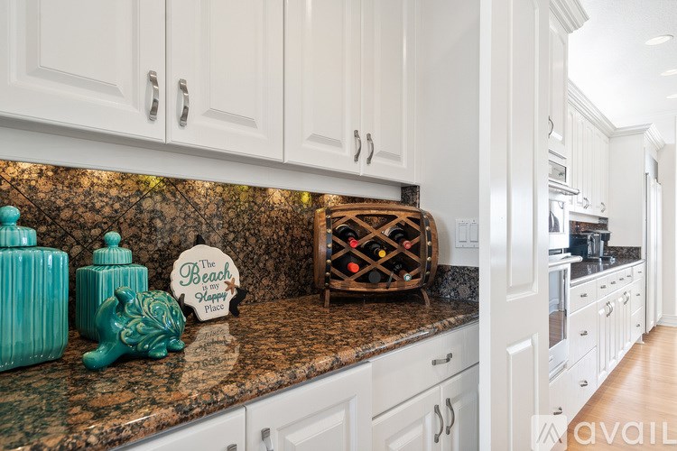 A kitchen with white cabinets and a granite countertop with a sign that says "The Beach".