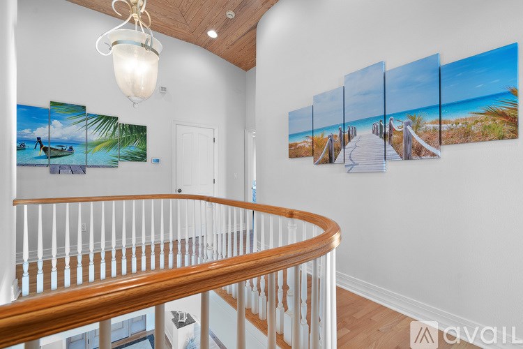 A staircase with a wooden banister and a chandelier hangs in a room with a wall of pictures.
