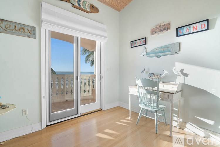 A room with a desk and chair, a window with a view of the beach, and a wall decorated with beach-themed items.
