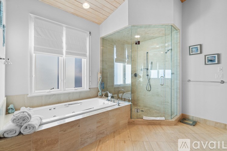 A bathroom with a glass shower stall and a bathtub with towels on it.