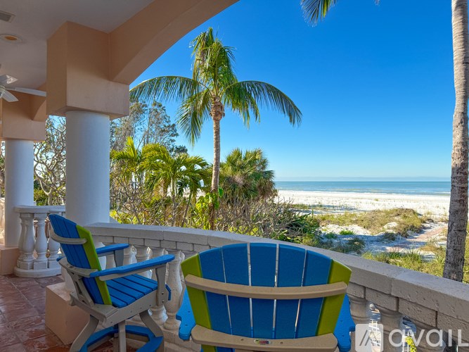 Two chairs are on a balcony overlooking the beach.