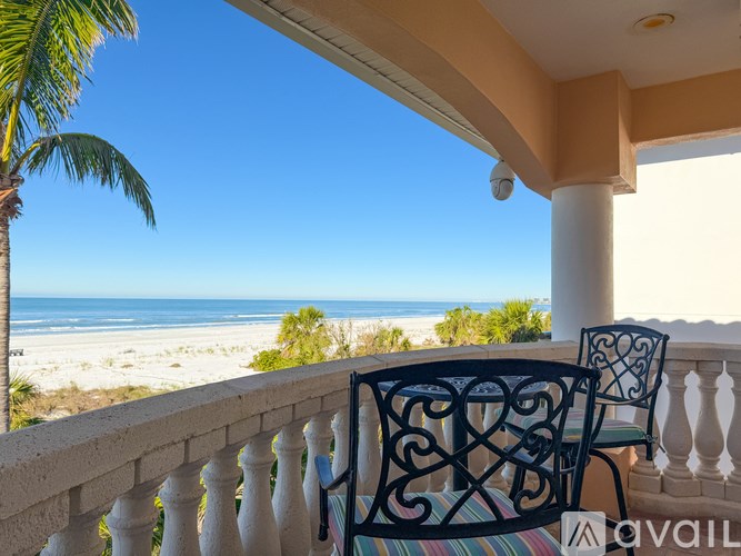 A balcony with two chairs and a table overlooking a beach.