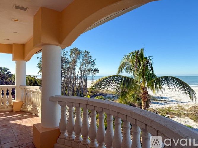 A balcony with a white railing overlooks a beach with palm trees.